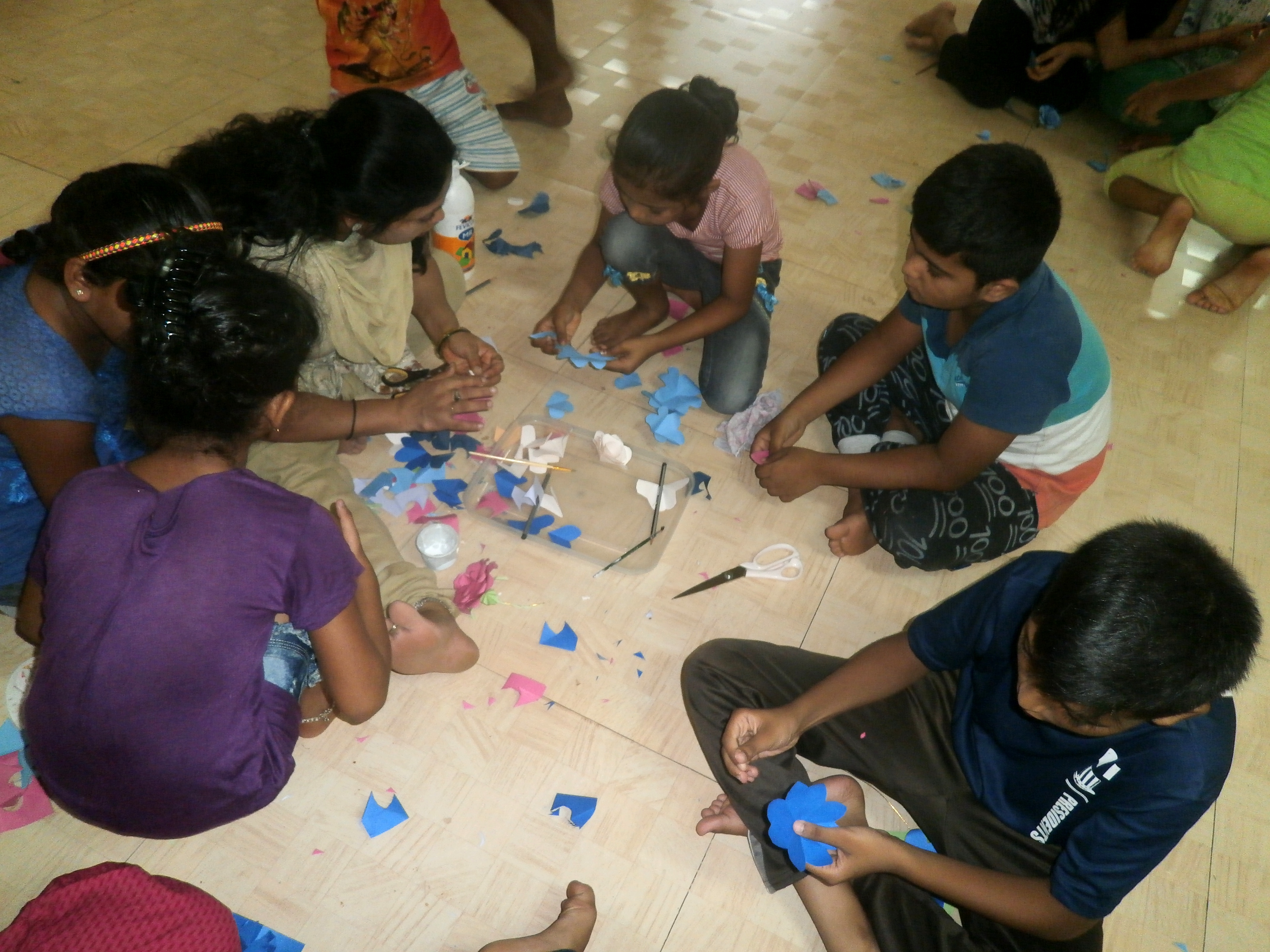 Children taking instructions from the teacher to make paper flowers
