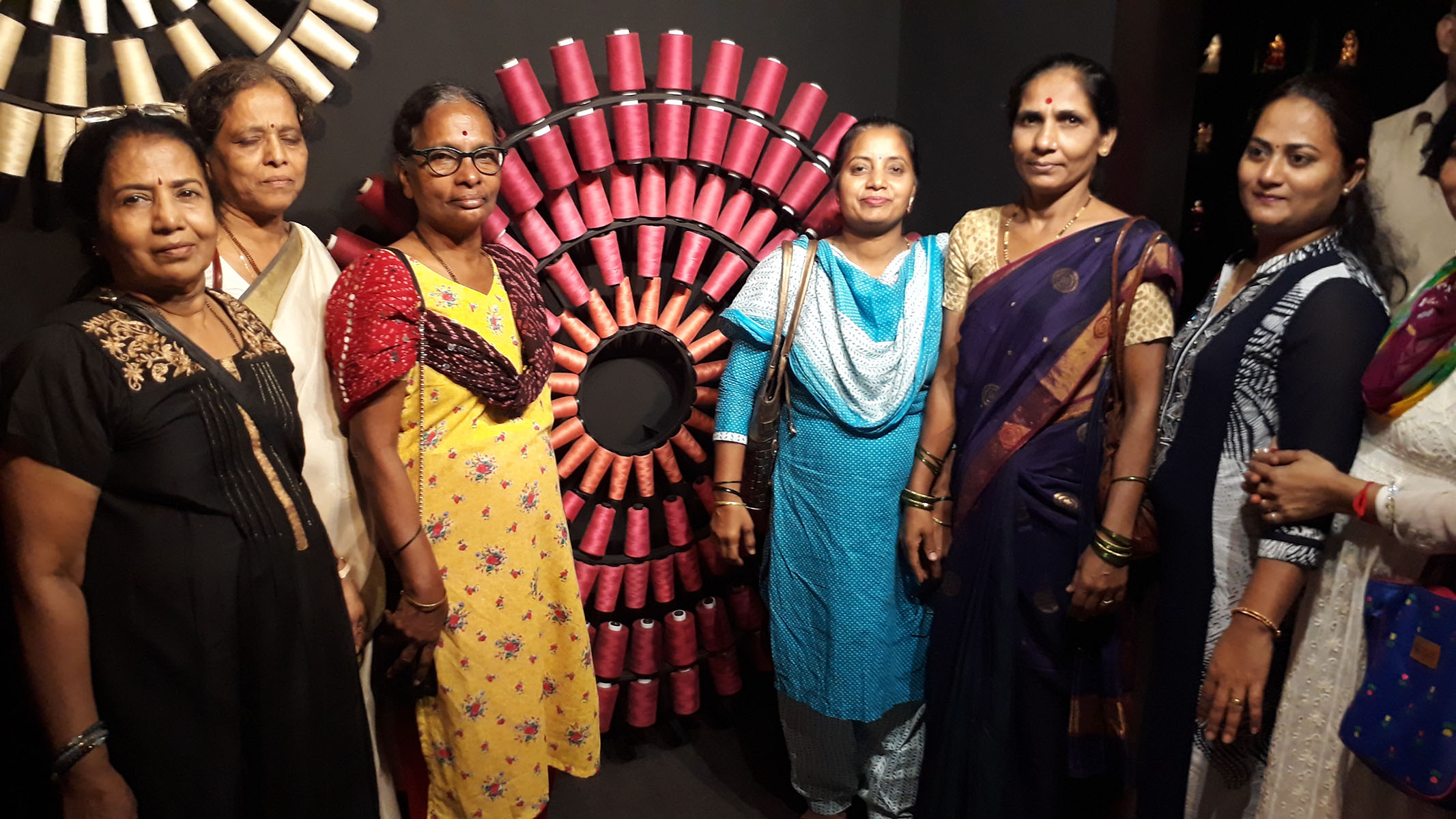 Few beneficiaries standing in front of an innovative model made of different thread roll
