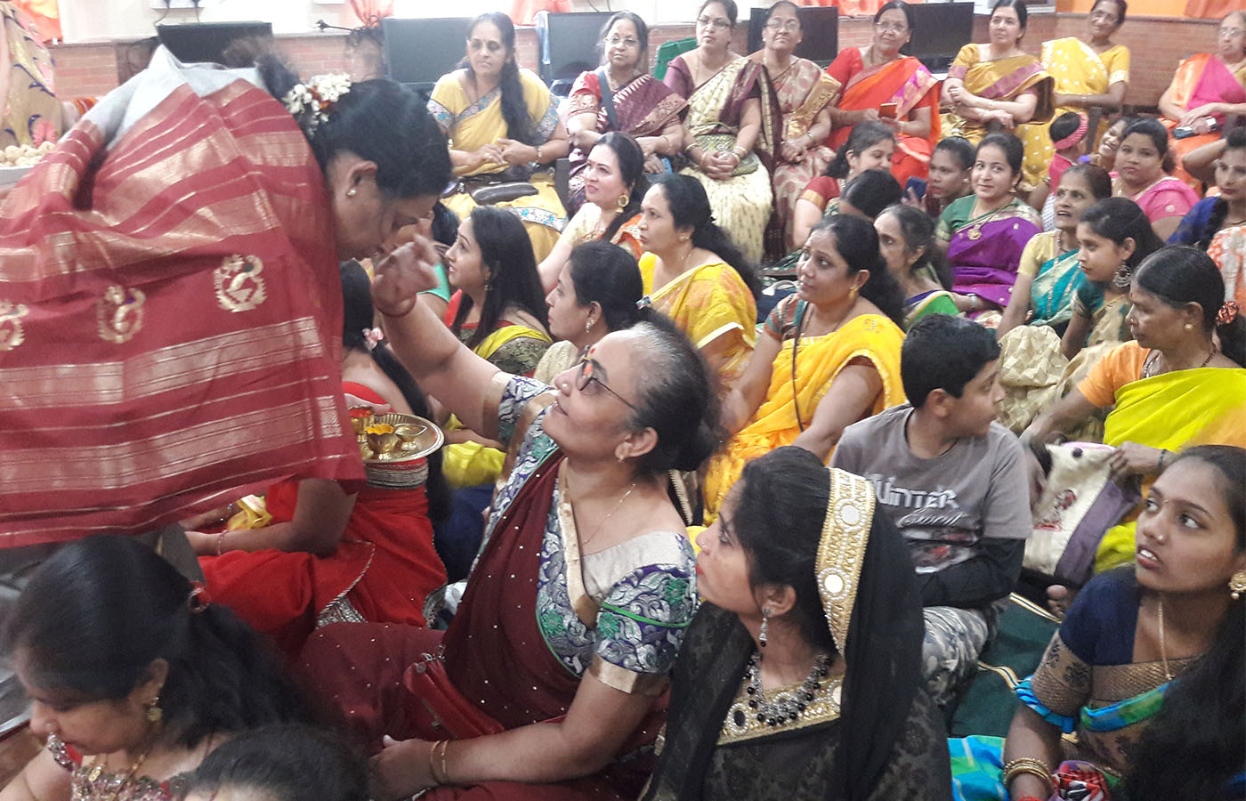 A beneficiary applying haldi and kumkum to a teacher that gifts a potted plant to her